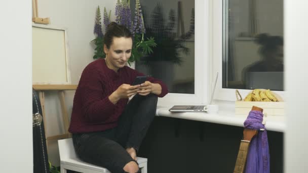 迷人的微笑的女人手拿智能手机坐在阳台上，看在线新闻，在社交媒体上聊天，打字 — 图库视频影像