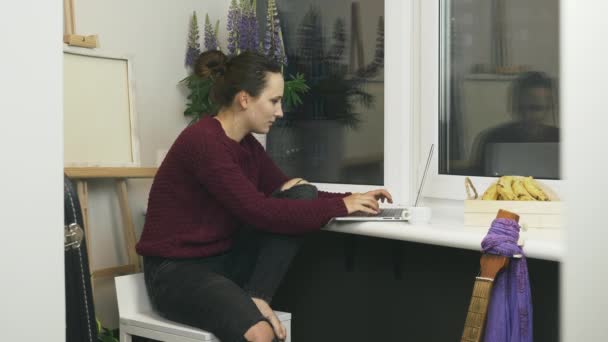 Mujer morena joven escribiendo en el teclado y el ordenador portátil de cierre sentado en la silla en el balcón. Freelancer mujer que trabaja en un cuaderno de estudio en casa. Mujer estudiante charlando en línea en las redes sociales — Vídeos de Stock