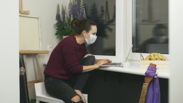 Mujer feliz se quita la mascarilla médica protectora y sonriendo mientras trabaja en el ordenador portátil desde el lugar de trabajo en el apartamento moderno. Trabajar desde casa durante el autoaislamiento y la cuarentena — Vídeos de Stock