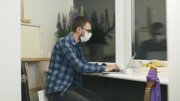 Étudiant masculin en masque facial médical de protection à l'aide d'un ordinateur portable sur le lieu de travail. Jeune homme fini de travailler sur ordinateur portable sur la distance. Travailler de la maison sur l'auto isolement pendant la quarantaine — Video