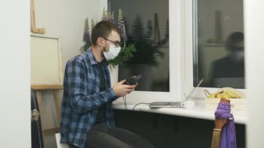 Gözlüklü genç adam ev işyerindeki balkonda dizüstü bilgisayarda çalışırken kulaklık takıyor ve müzik dinliyor. Kulaklık takan, müzik dinleyen ve internetten okuyan erkek öğrenci.