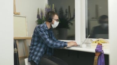 Koruyucu maskeli bir adam internet kamerasıyla video görüşmesi yapıyor ve karantina sırasında evde tek başına kalan aile ve arkadaşlarıyla konuşuyor. Çevrimiçi grup görüntülü konuşma konferansı yapan serbest çalışan erkek.