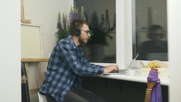 Mann nimmt Kopfhörer nach der Arbeit am Laptop von zu Hause ab. Männliche Schüler, die nach der Hausaufgabenbetreuung auf dem Notebook die Kopfhörer abnehmen. Freiberufler beendet seine Arbeit an einem Remote-Projekt am heimischen Arbeitsplatz — Stockvideo