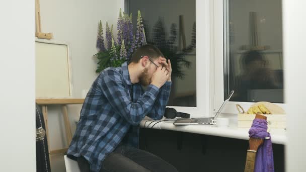 El hombre cansado y molesto se quita las gafas y se preocupa por los errores en el trabajo sentado en el balcón en el acogedor estudio de casa moderna. Joven malestar masculino con resultados financieros en los mercados financieros . — Vídeos de Stock