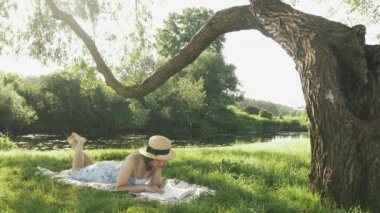 Genç bir kadın yazı nehir kenarındaki parkta, ağacın altında çimlere uzanıp edebiyat okuyarak ve dinlenerek geçiriyor. Parkta dinlenen elbiseli bir kız. Hafta sonu kırsalda bir kadın