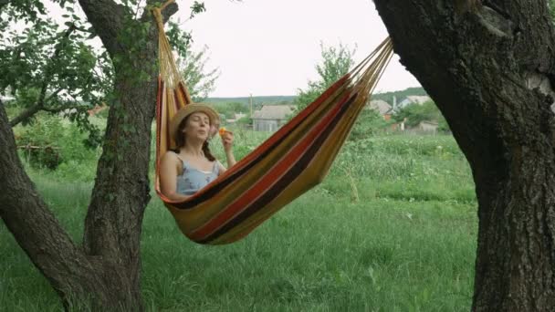 Donna in amaca è soffia bolle all'aperto. Giovane ragazza in cappello e vestito sdraiato in amaca e soffiando bolle, riposo e relax in campagna nel fine settimana — Video Stock