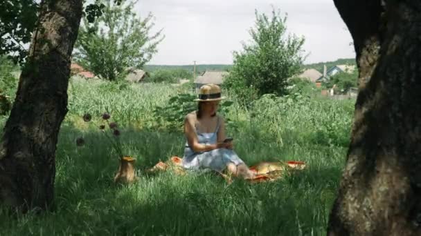 Femme avec smartphone dans le parc. Femme utilisant un téléphone portable au jardin vert. Fille assise sur l'herbe dans le parc et tapant sur smartphone. Femme passant du temps dans un parc vert en vacances d'été — Video