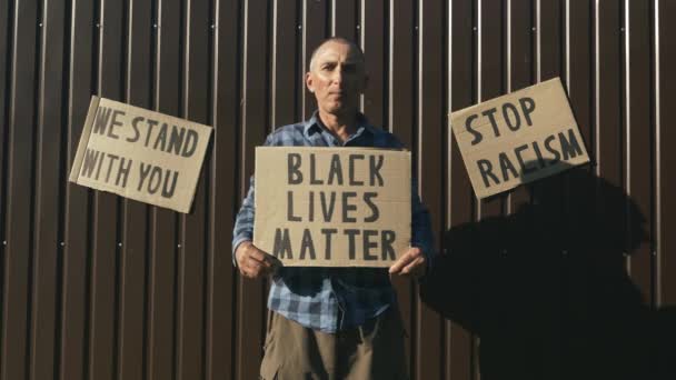 Póster BLACK LIVES MATTER en manos del viejo hombre caucásico. Detener el concepto de racismo. El hombre sostiene el cartel "La vida de los negros importa". Manifestaciones contra el racismo anti-negro y la brutalidad policial — Vídeos de Stock