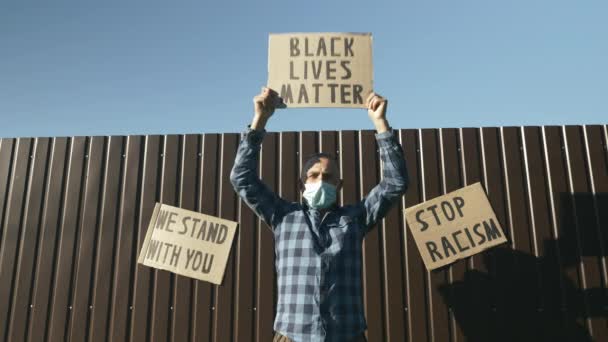 Viejo hombre caucásico coreando con el letrero "La vida de los negros importa" en las manos en una sola protesta pacífica contra el racismo negro. Cartel de ondulación masculina senior: LA VIDA NEGRA IMPORTA en las manos contra la pared marrón y el cielo azul — Vídeos de Stock