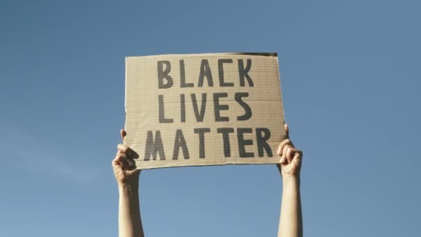 Знак BLACK LIVES MATTER проти блакитного неба. Жінка розмахує плакатом "Чорне життя має значення". Мітинги проти політичної жорстокості та античорного расизму. Руки проти блакитного неба, що тримає знак BLACK LIVES MATTER — стокове відео