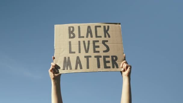 Signer BLACK LIVES MATTER contre le ciel bleu. Les mains de la femme agitant l'affiche "Black lives matter". Rassemblement contre la brutalité policière et le racisme anti-noir. Les mains contre le ciel bleu tenant signe BLACK LIVES MATTER — Video