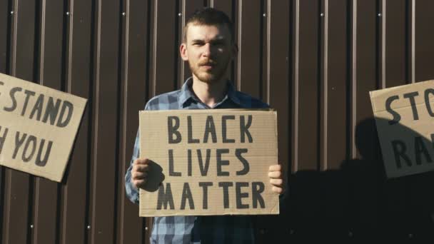 Portret van een jonge blanke man met bord "Black lives matter" in handen. Rally tegen politiegeweld. Stop racisme. Poster "Black lives matter" in handen van de mens. Vreedzaam protest tegen zwart racisme — Stockvideo
