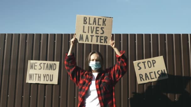 Mulher na máscara de cara protetora que mantém o sinal "A matéria de vidas preta" em mãos contra parede marrom e céu azul. Cartaz "Vidas negras importam" nas mãos. Pára com o racismo. Comícios contra o racismo e a brutalidade policial — Vídeo de Stock