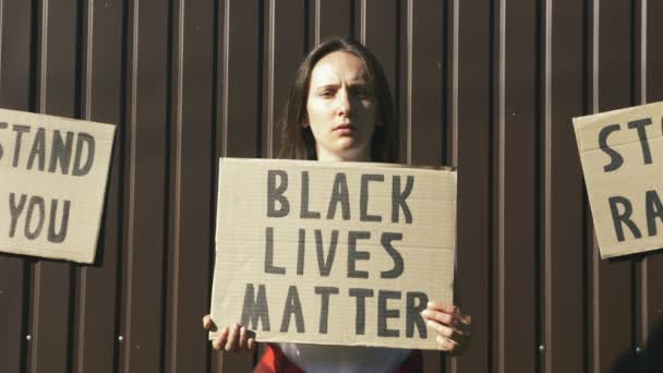 Retrato de una joven mujer caucásica sosteniendo el letrero "Las vidas de los negros importan" en manos sobre fondo marrón. Reuniones contra el racismo y la brutalidad policial. Detener el racismo — Vídeos de Stock