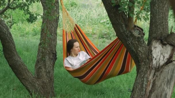 Mulher deitada na rede. Jovem mulher relaxando na rede no verão. Menina descansando no campo . — Vídeo de Stock