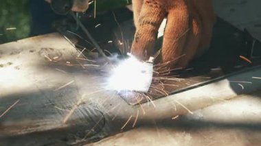 Eller metal çelik ve demirle kaynak makinesini kullanarak çalışıyor. Metal kaplama için elektrikli kaynak makinesi kullanan bir adam. Parlak kıvılcımlar ve parıltılar