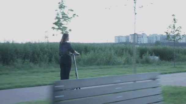 Chica se mueve en scooter eléctrico ecológico en el terraplén de la ciudad al atardecer. Joven mujer de negocios en traje monta en e-scooter desde la oficina. Mujer montando transporte eléctrico personal en el paseo al atardecer — Vídeo de stock