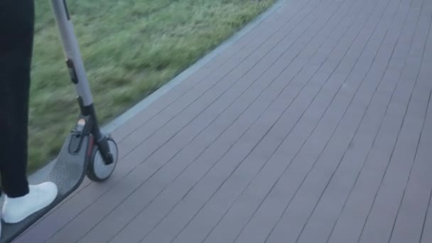 Donna moderna che utilizza scooter elettrico sulla strada della città. Primo piano di gambe donna cavalcando carico trasporto ecologico personale. Ragazza cavalca scooter indossando pantaloni neri e scarpe da ginnastica bianche. Stile di vita sano — Video Stock