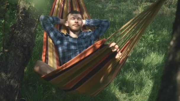 Hombre durmiendo en hamaca al aire libre. Hombre despreocupado relajándose en la hamaca en el día soleado del verano. Guapo turista masculino disfrutando de vacaciones en hamaca en el campo — Vídeo de stock