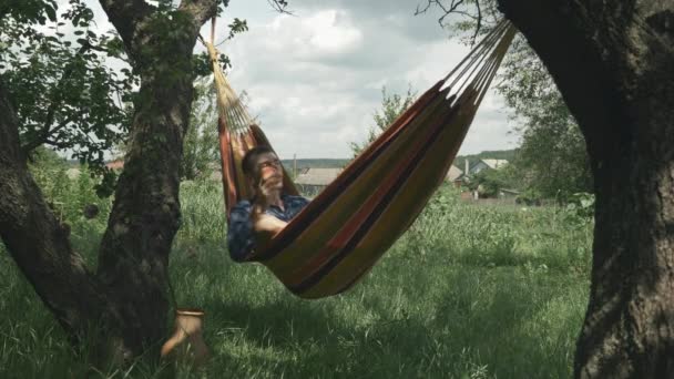 L'uomo rilassato che gode la vacanza in hammock al giardino verde. Giovane maschio in amaca in estate giornata di sole. L'uomo casuale si rilassa sul hammock all'aperto. Bello maschio rilassante in amaca in campagna — Video Stock