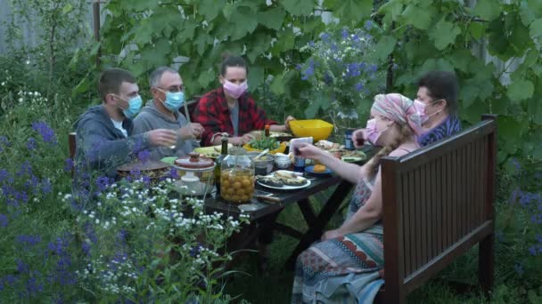 村の夏の家でピクニックで保護医療マスクの家族。中庭で一緒に休日を祝う人々の会社。大きな家族のパーティーは屋外で祝います。親戚同士で — ストック動画