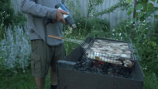男は庭の乾燥機を使って火をおこす。グリルで石炭を粉砕します。炭火をバーベキューグリルで焼く。石炭が燃焼し始めている。たき火の料理。外の夏のピクニック — ストック動画