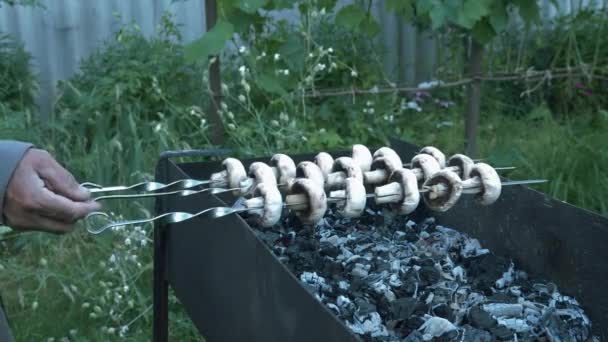 O homem transforma espetos de cogumelos. Homem a cozinhar vegetais grelhados lá fora. Preparando churrasco ao ar livre. Produtos hortícolas na grelha — Vídeo de Stock