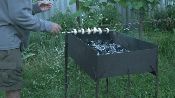 Skewers van paddenstoelen. Gegrilde paddenstoelen. De man doet spiesjes groente op het vuur. Groenten op open vuur. Barbecue op de grill. Bereiden van gegrilde groenten buiten — Stockvideo