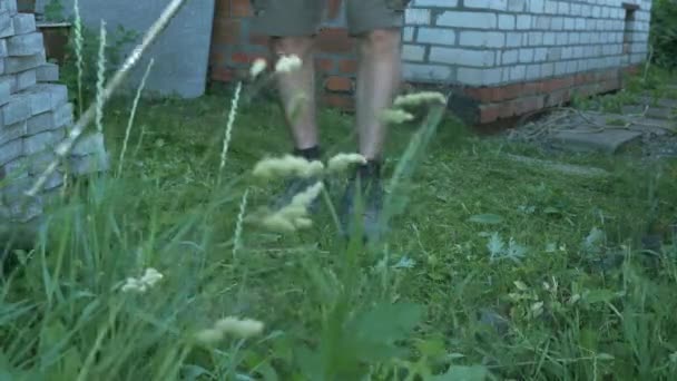 L'uomo giardiniere falcia l'erba sul prato usando il tosaerba a benzina. Maschio falcia erba alta verde, tenendo in mano piccolo tosaerba. Erba che vola in direzioni diverse. Uomo che taglia erba con tosaerba — Video Stock