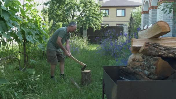 Mann hackt Brennholz für die Zubereitung von Grill oder Grill auf dem grünen Hof. Holzfäller mit Axt hackt Brennholz. Mann in Freizeitkleidung hackt Holz mit Axt draußen. Mann hackt Holzklotz mit großer Axt — Stockvideo