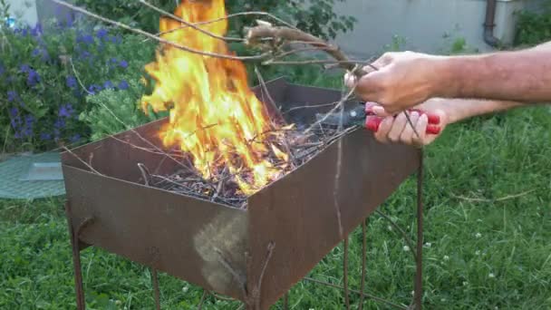 Hombre haciendo llamas de fuego para preparar la parrilla. Llamas de los árboles para la parrilla o barbacoa. Carbón en llamas en parrilla de barbacoa. Hombre organizando una pequeña hoguera afuera para preparar la parrilla — Vídeo de stock