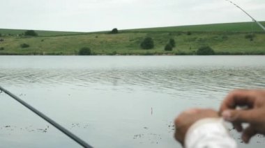 Balıkçı elleri balıkçılık için olta takımı hazırlıyor. Dönmek için kanca. Olta kamışlı erkek eller. Erkek balıkçı, nehrin arka planında olta tutuyor. Dönen olta, elinde makarayla.