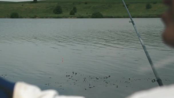 Kalastus kelluu järvellä tai jokivedessä. Kalastaja kalastaa veneessä joen rannalla. Mies pyydystää kalaa järvellä. Jokikalastus lähellä rantaa. Kalastajan elämäntavan käsite — kuvapankkivideo