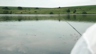 Balıkçı nehirde ya da gölde balık yakalar. Açık havada erkek avcılığı. Suyun üzerindeki olta kamışı. Balıkçı teknesini kapatın. Nehir kıyısında balık tutan adam