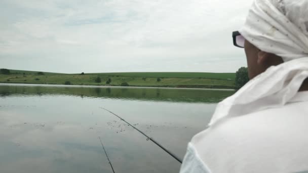 Pescador com vara de pesca sentado perto da costa do rio. Homem pega peixe ao ar livre. A pescar no lago. Recreação na pesca no fim de semana. Estilo de vida dos pescadores. Masculino relaxa com vara de pesca no lago — Vídeo de Stock