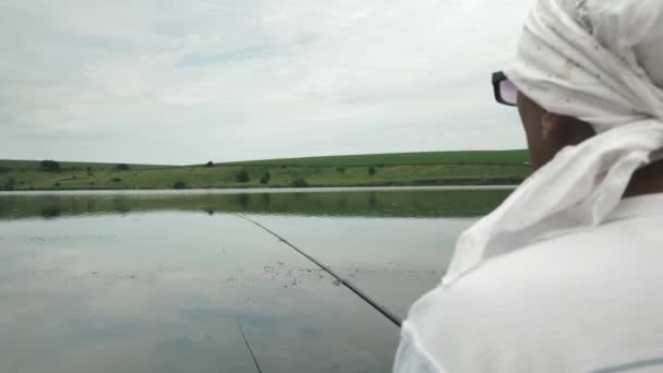 Człowiek łowiący ryby nad jeziorem. Rybak siedzi przy brzegu rzeki i łowi ryby. Wędkowanie na świeżym powietrzu. Rybak łowi ryby wędką — Wideo stockowe