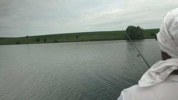 Człowiek łowi ryby w zbiorniku. Rybak łowiący ryby z wędkami na jeziorze. Koncepcja stylu życia rybaka. Rybołówstwo rzeczne w pobliżu brzegu w letni słoneczny dzień — Wideo stockowe