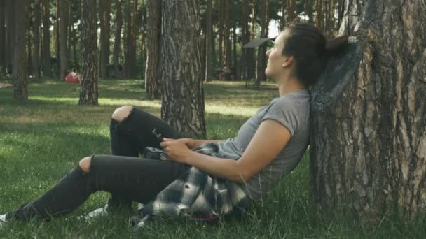 Portrait of young brunette woman relaxing with skateboard in park at sunset. Hipster girl skateboarder having fun in park — Stock Video