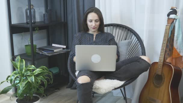 Femme tapant sur le clavier d'ordinateur portable à partir du bureau à la maison. Femme assise sur une chaise moderne confortable et travaillant sur un ordinateur portable. Fille détente dans la chaise avec ordinateur portable. Bureau à domicile. Travail à domicile — Video