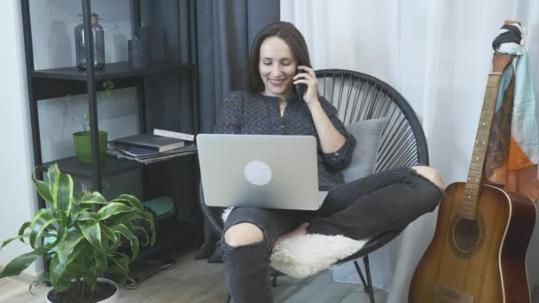 Junge Geschäftsfrau telefoniert zu Hause im Büro. Glücklich lächelnde, per Smartphone sprechende Frau sitzt auf einem Sessel in einer gemütlichen modernen Wohnung. Freiberuflerin arbeitet von zu Hause aus und telefoniert — Stockvideo