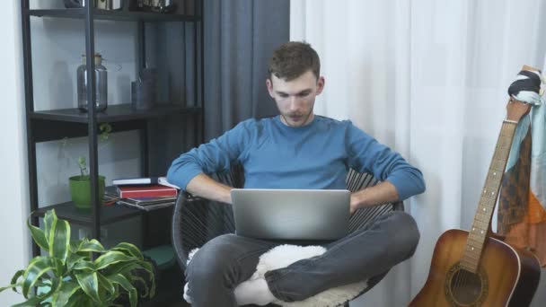 Giovane freelance di sesso maschile finire di lavorare sul computer portatile a casa ufficio. Uomo rilassante sulla sedia in appartamento moderno. L'uomo d'affari lavora sul taccuino sulla sedia. Programmatore maschio che lavora su laptop a casa — Video Stock