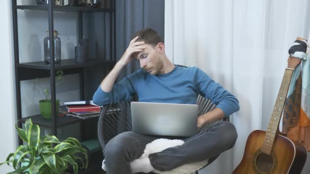 Hombre cansado trabajando en la computadora portátil en la silla en la oficina en casa. Joven hombre de negocios cansado en el trabajo en casa oficina. Hombre freelancer trabajando en la computadora, cansado y molesto. El hombre decepcionado trabaja en el portátil — Vídeos de Stock