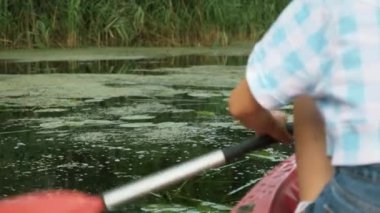 Suda kano küreği, yakın çekim. Genç gezgin kadın yazın sakin bir nehirde kanoda kürek çekiyor. Dişi turist tatilde teknede yüzer. Kız gölü keşfediyor ve kanoyla seyahat ediyor.