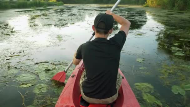 男は夏に穏やかな池のカヌーに浮かんでいる。カヤックで強力な男性探検家川。スポーツ・ローイング。男性観光客は日没時に静かな湖でカヤックです。若いアクティブな旅行者がボートでラフティングしている — ストック動画