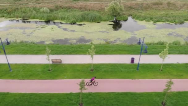 Athletic cyclist is riding fast on road bicycle along cycle path in summer. Young fitness female is cycling on bike along river. Woman rides on bike in park. Professional athlete is training on bike — Stock Video