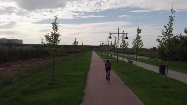 Professional female cyclist in cycling apparel and black helmet is riding on road bike on bicycle path along river. Young brunette woman is cycling on bicycle in park. Triathlon and sport concept — Stock Video