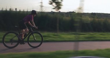 Bisikletli kadın eyerden hızla iniyor, pedalları yukarı itiyor ve sıkı çalışıyor. Profesyonel triatlet gün batımında bisikletle hız yapıyor. Zor bisiklet egzersizi. Parkta kadın motorsiklet sürüyor.