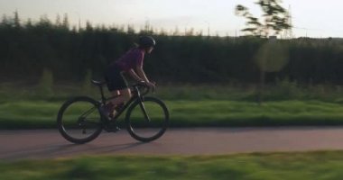 Profesyonel bayan bisikletçi gün batımında aero motorla yolda hız yapıyor. Genç sportif formda kadın gün ışığında bisikletle pedal çeviriyor. Esmer kız park yolunda bisiklet sürüyor.