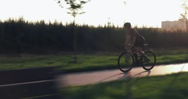 In forma bella donna sta pedalando veloce su aero bike al tramonto. Atletica ragazza sportiva è in bicicletta sulla pista ciclabile nel parco. ciclista femminile è l'allenamento sul ciclo e fare esercizi di allenamento all'aperto — Video Stock