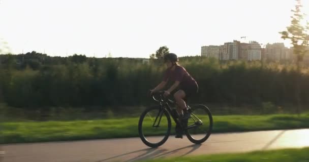 Donna ciclista sta cavalcando lungo la bella strada ciclabile tra i campi. Allenamento atletico o di forza al tramonto. Stile di vita ciclistico sano. Atleta femminile sta prendendo il comando in bicicletta al tramonto — Video Stock